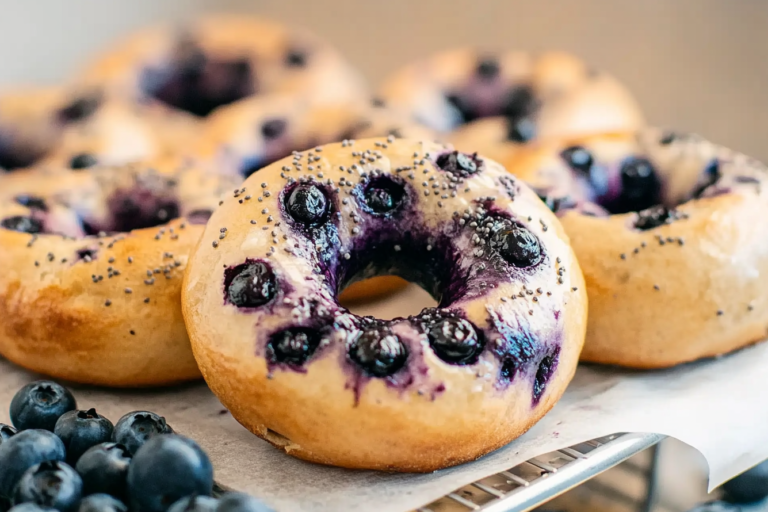 Freshly baked blueberry bagel recipe on a wooden board, showcasing golden crusts and juicy blueberries.